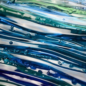 May include: Abstract artwork featuring flowing lines of blue, teal, and white. The glossy surface has a textured appearance with small, droplet-like details. The color palette evokes a sense of water and movement.