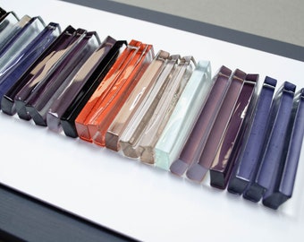 May include: A framed art piece featuring a row of glass tiles in various shades of purple, blue, gray, brown, orange, and red.