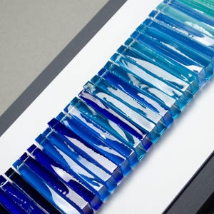May include: A wall art piece made of glass tiles in shades of blue, teal, and green. The tiles are arranged in a gradient pattern, creating a wave-like effect.