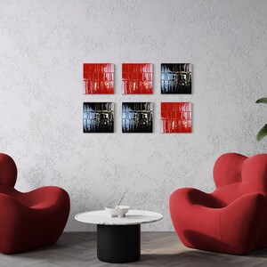 May include: Six square wall art pieces in red and black are displayed on a textured white wall. Two red armchairs and a round table with a black base are in front of the wall. A potted plant is on the right.