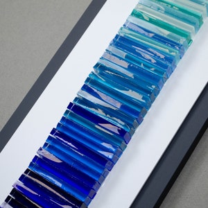 May include: A framed wall art piece featuring a gradient of blue and green glass tiles arranged vertically.