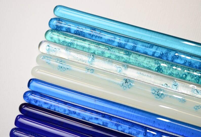 Pu&ograve; includere: Un set di dieci bacchette di vetro in varie tonalit&agrave; di blu, dal blu scuro al blu chiaro, con bolle d'aria intrappolate al loro interno. Le bacchette sono disposte in un motivo sfumato, con il blu pi&ugrave; scuro in basso e il blu pi&ugrave; chiaro in alto.