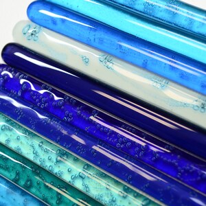 May include: A collection of glass rods in various shades of blue and green, with air bubbles trapped inside. The rods are arranged in a gradient pattern, starting with the darkest blue at the bottom and transitioning to the lightest green at the top.