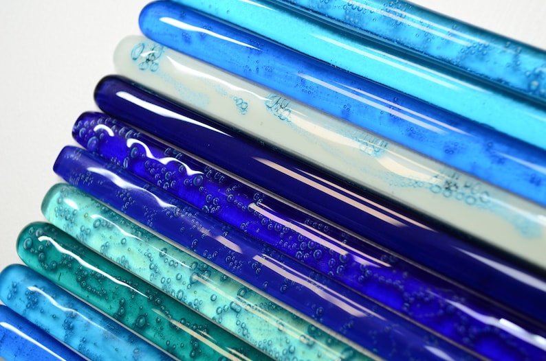 May include: A collection of glass rods in various shades of blue and green, with air bubbles trapped inside. The rods are arranged in a gradient pattern, starting with the darkest blue at the bottom and transitioning to the lightest green at the top.