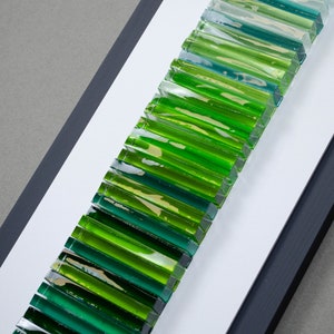 May include: A framed wall art piece featuring a gradient of green and blue glass tiles arranged vertically.