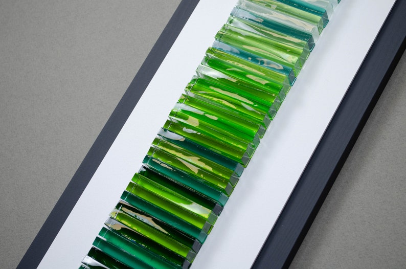 May include: A framed wall art piece featuring a gradient of green and blue glass tiles arranged vertically.