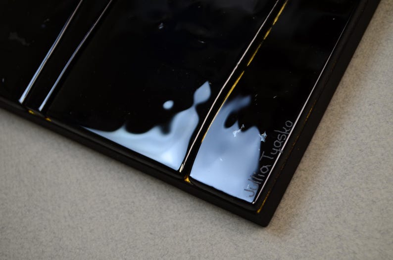 May include: Close-up of a rectangular black tray with a glossy finish. The tray has a series of parallel grooves and a small inscription that reads "Julia Tyasko". The tray is on a light grey surface.