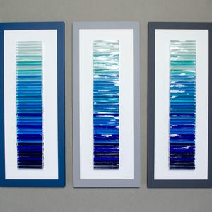 May include: Three framed wall art pieces with a gradient of blue glass tiles. The tiles are arranged vertically in each frame, creating a visual representation of a blue ocean.
