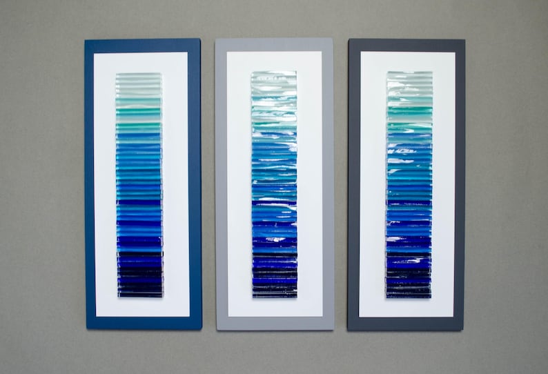 May include: Three framed wall art pieces with a gradient of blue glass tiles. The tiles are arranged vertically in each frame, creating a visual representation of a blue ocean.