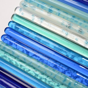Pu&ograve; includere: Primo piano di un'opera d'arte murale realizzata con bacchette di vetro in varie tonalit&agrave; di blu, turchese e bianco. Le bacchette di vetro sono disposte in un motivo sfumato, creando un effetto visivo di acqua.