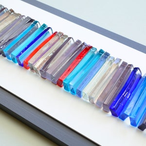 May include: A framed wall art piece featuring a row of colorful glass tiles in various shades of blue, red, and gray.