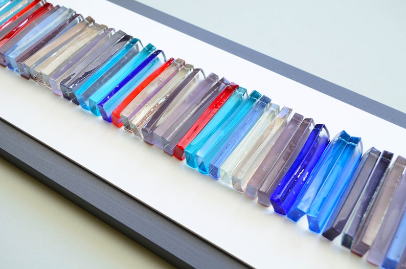 May include: A framed wall art piece featuring a row of colorful glass tiles in various shades of blue, red, and gray.