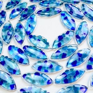 May include: A collection of blue and clear glass tiles in a leaf shape. The tiles are arranged in a spiral pattern.