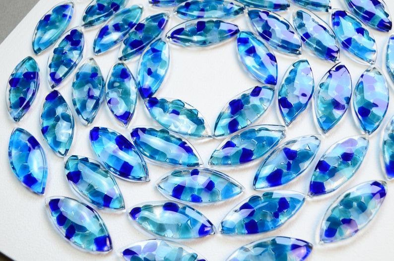 May include: A collection of blue and clear glass tiles in a leaf shape. The tiles are arranged in a spiral pattern.
