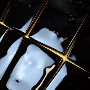 May include: Close-up of glossy black rectangular tiles with gold-coloured grout lines. The tiles reflect light, creating a pattern of highlights and shadows. The overall effect is a modern, geometric design.