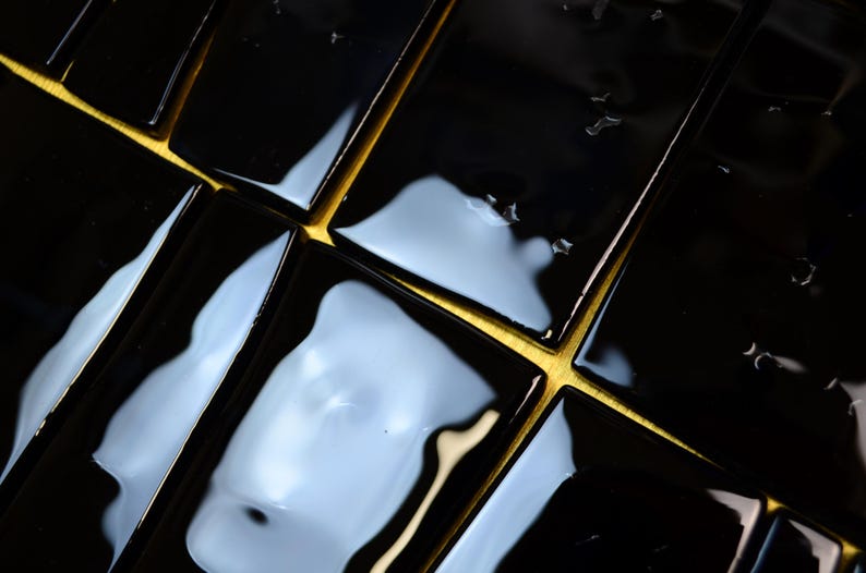 May include: Close-up of glossy black rectangular tiles with gold-coloured grout lines. The tiles reflect light, creating a pattern of highlights and shadows. The overall effect is a modern, geometric design.