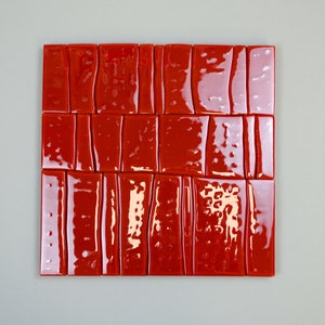 May include: A square arrangement of glossy, rectangular red tiles. The tiles are arranged in a grid pattern, with each tile having a slightly irregular shape and a reflective surface. The tiles are a vibrant shade of red.