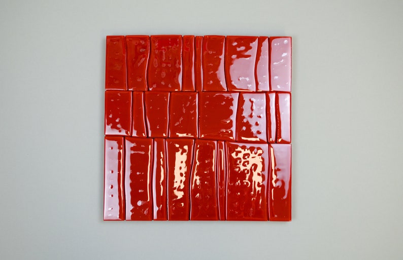 May include: A square arrangement of glossy, rectangular red tiles. The tiles are arranged in a grid pattern, with each tile having a slightly irregular shape and a reflective surface. The tiles are a vibrant shade of red.