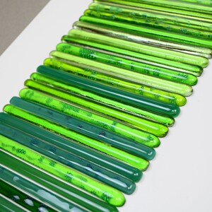 May include: A wall art piece made of green glass rods arranged in a gradient pattern, starting with a light green and transitioning to a dark green.