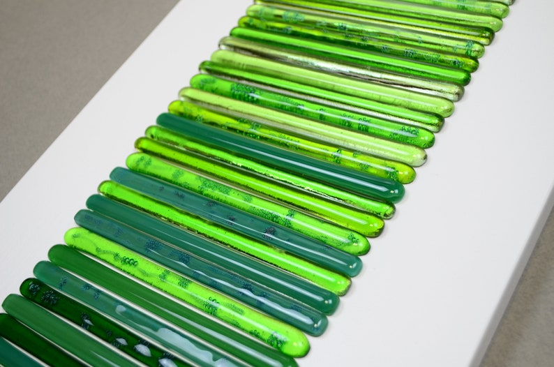 May include: A wall art piece made of green glass rods arranged in a gradient pattern, starting with a light green and transitioning to a dark green.