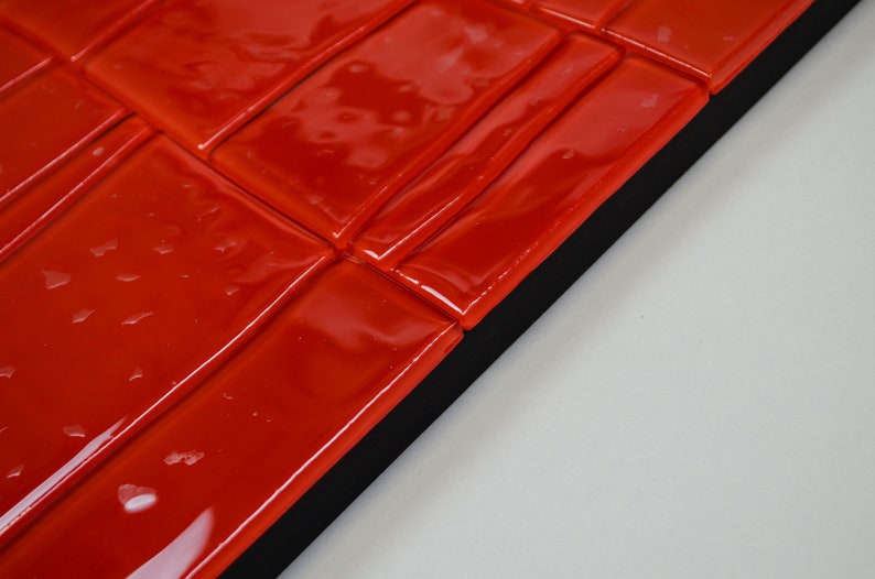 May include: Close-up of a section of red glossy tiles arranged in a brick pattern. The tiles are rectangular and have a reflective surface. The tiles are set against a black border and a white background.