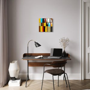 May include: An abstract artwork with a rectangular design, featuring a grid of colourful blocks. The blocks include shades of yellow, blue, red, and brown. The artwork hangs above a desk with a laptop, lamp, and chair, creating a modern office setting.