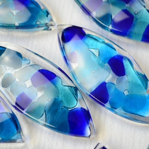 May include: A set of six blue and white glass ornaments shaped like teardrops. The ornaments are filled with small pieces of glass in shades of blue and white.