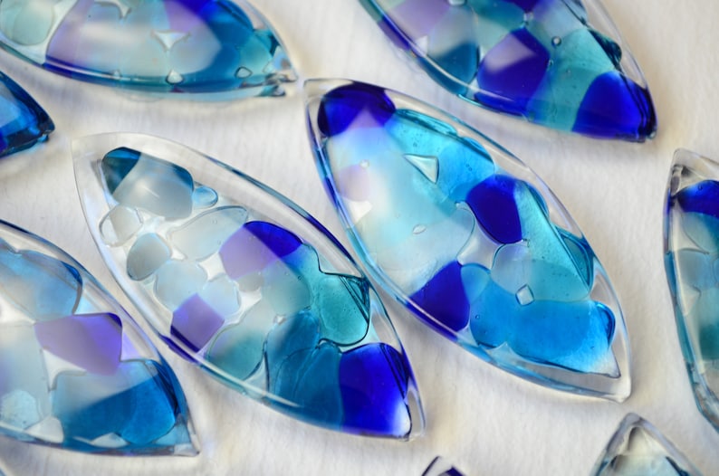 May include: A set of six blue and white glass ornaments shaped like teardrops. The ornaments are filled with small pieces of glass in shades of blue and white.