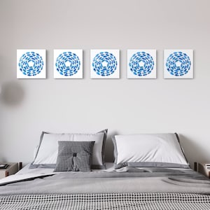 May include: Five square blue and white abstract art prints with a circular design, hanging on a white wall above a gray bed with white bedding and a gray throw blanket.