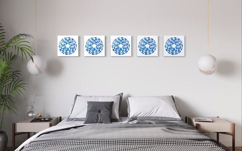 May include: Five square blue and white abstract art prints with a circular design, hanging on a white wall above a gray bed with white bedding and a gray throw blanket.