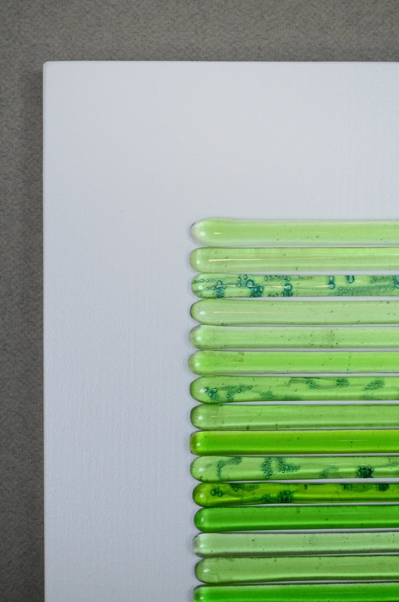 May include: A wall art piece made of green glass tubes arranged in a vertical line. The tubes are of varying lengths and have a slightly textured surface.