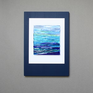 May include: A framed abstract art piece with a blue and white color scheme. The artwork is made of layered glass and resembles a seascape.