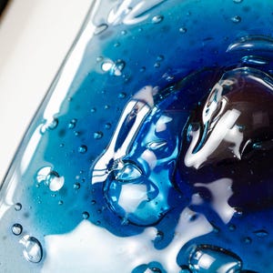 May include: A rectangular glass plate featuring a gradient of deep cobalt blue to lighter turquoise tones. The surface is characterized by numerous trapped air bubbles of varying sizes, creating a textured, liquid-like appearance with high gloss.
