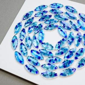 May include: A circular arrangement of blue and teal glass pieces, each shaped like an oval, on a white background.
