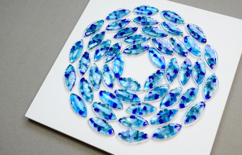 May include: A circular arrangement of blue and teal glass pieces, each shaped like an oval, on a white background.