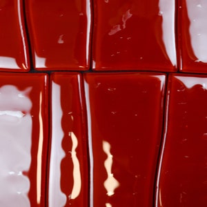 May include: Close-up of a glossy, rectangular tile pattern. Alternating red and white tiles create a striking visual effect. The tiles are arranged in a grid, with dark lines separating each piece. The reflective surface enhances the vibrant colours.