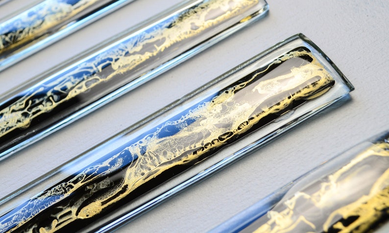 May include: Four clear glass tiles with black and gold marbling inside. The tiles are arranged in a row, with the top tile slightly offset from the others.