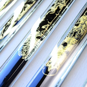 May include: Close-up of several glass tubes filled with black and gold liquid. The tubes are arranged in a row, and the liquid inside each tube has a different pattern.