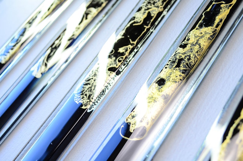 May include: Close-up of several glass tubes filled with black and gold liquid. The tubes are arranged in a row, and the liquid inside each tube has a different pattern.