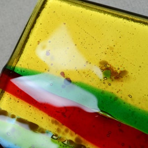 K&ouml;nnte beinhalten: Eine rechteckige Glasschale mit einem gestreiften Design in Gelb, Gr&uuml;n, Rot und Blau. Das Glas hat kleine Luftblasen.