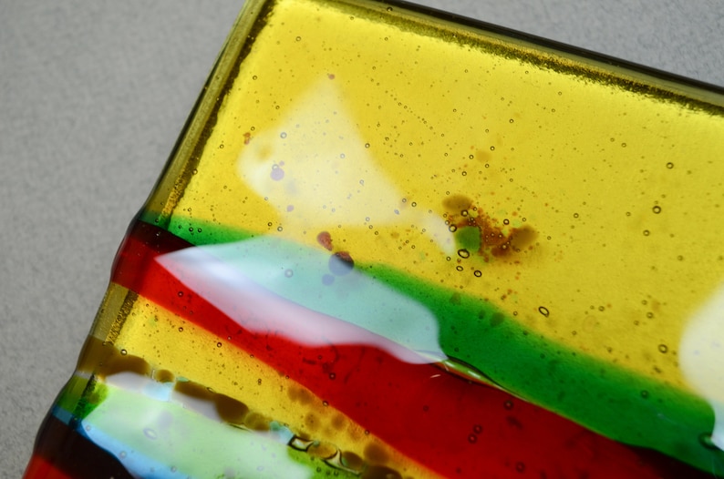 K&ouml;nnte beinhalten: Eine rechteckige Glasschale mit einem gestreiften Design in Gelb, Gr&uuml;n, Rot und Blau. Das Glas hat kleine Luftblasen.