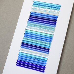 Pu&ograve; includere: Un'opera d'arte da parete realizzata con bacchette di vetro in varie tonalit&agrave; di blu, dal blu chiaro al blu scuro, disposte in uno schema verticale.
