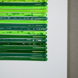 May include: A white surface with a series of green glass rods arranged in a vertical line. The rods are different shades of green, from light to dark.