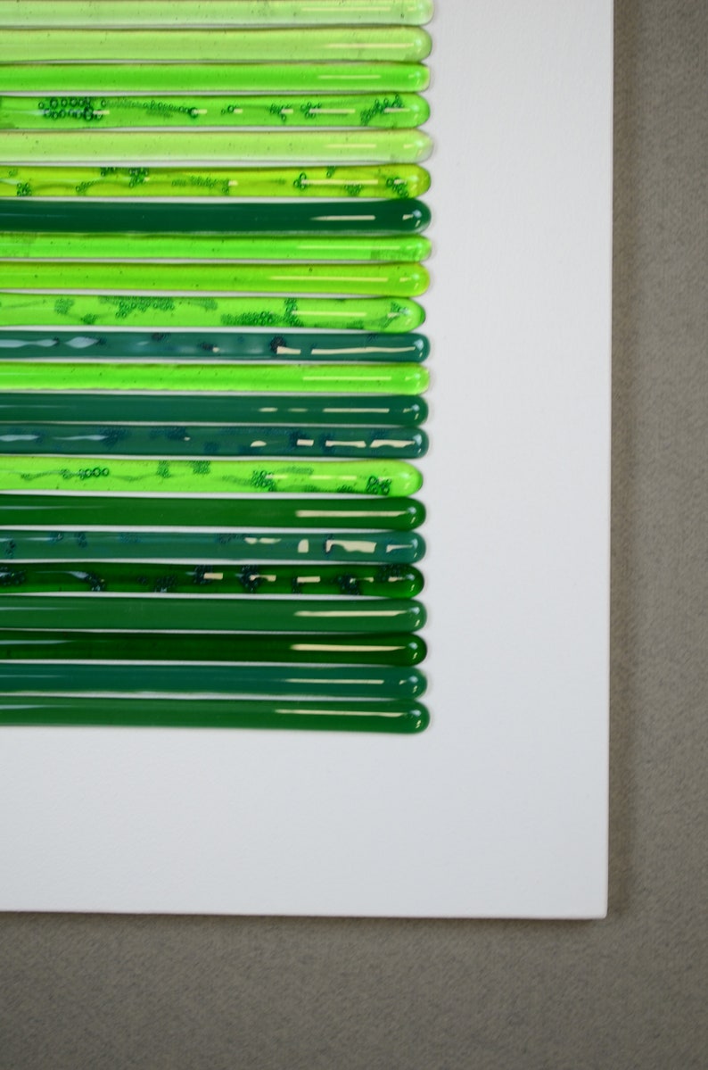 May include: A white surface with a series of green glass rods arranged in a vertical line. The rods are different shades of green, from light to dark.