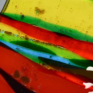 K&ouml;nnte beinhalten: Nahaufnahme eines bunten Glaskunstwerks mit Schichten aus rotem, gr&uuml;nem, blauem und gelbem Glas. Das Glas hat eine strukturierte Oberfl&auml;che mit kleinen Luftblasen, die darin eingeschlossen sind.