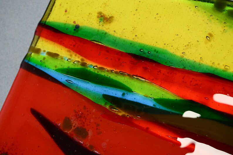K&ouml;nnte beinhalten: Nahaufnahme eines bunten Glaskunstwerks mit Schichten aus rotem, gr&uuml;nem, blauem und gelbem Glas. Das Glas hat eine strukturierte Oberfl&auml;che mit kleinen Luftblasen, die darin eingeschlossen sind.