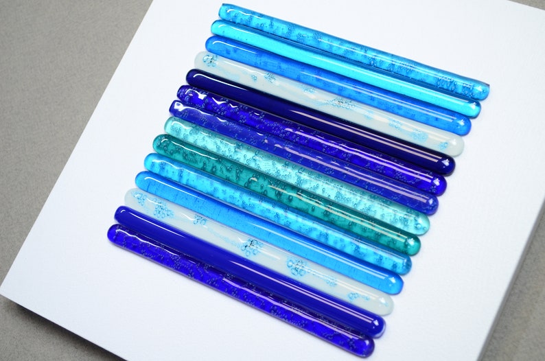 May include: A wall art piece made of glass rods in various shades of blue, from teal to dark blue, arranged in a graduated pattern.