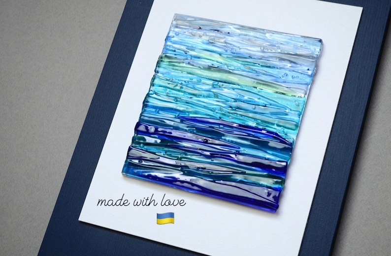 May include: A framed artwork featuring a blue and green glass mosaic with a horizontal striped pattern. The artwork is framed in a dark blue frame and has the text "made with love" and a Ukrainian flag printed below the mosaic.