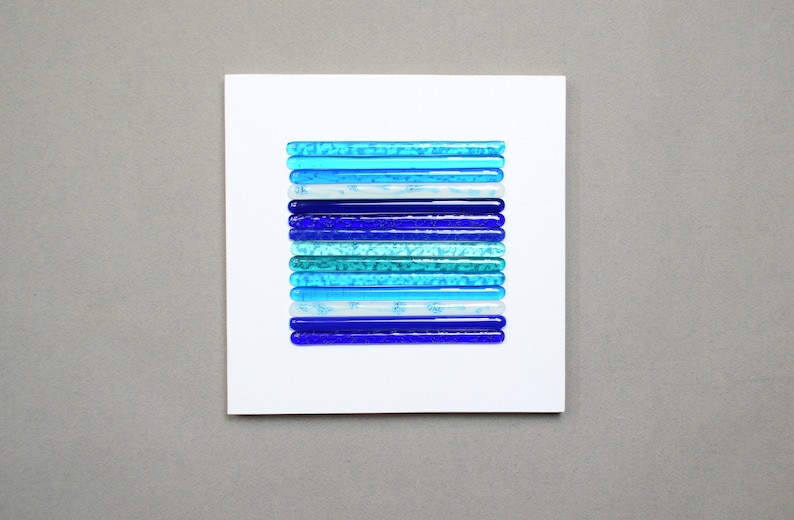 May include: A white card with a blue and white glass mosaic art piece. The mosaic is made of small, rectangular pieces of glass in shades of blue, turquoise, and white. The pieces are arranged in horizontal rows, creating a gradient effect from dark blue to light blue.