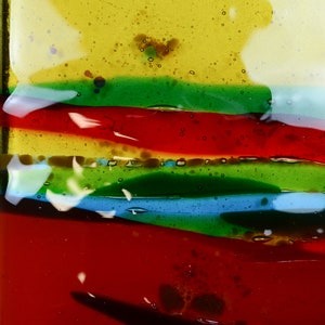 K&ouml;nnte beinhalten: Nahaufnahme eines bunten Glaskunstwerks mit Schichten aus rotem, gr&uuml;nem, blauem und gelbem Glas. Das Glas hat eine strukturierte Oberfl&auml;che und scheint handgefertigt zu sein.